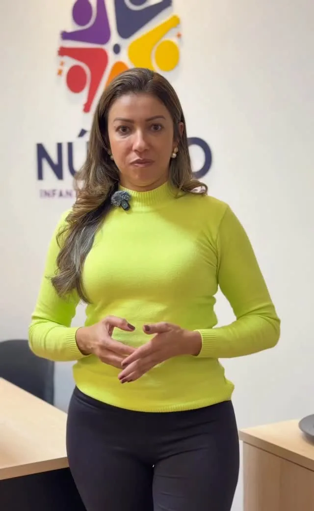 Profissional do Núcleo diante da parede com o logo colorido da clínica